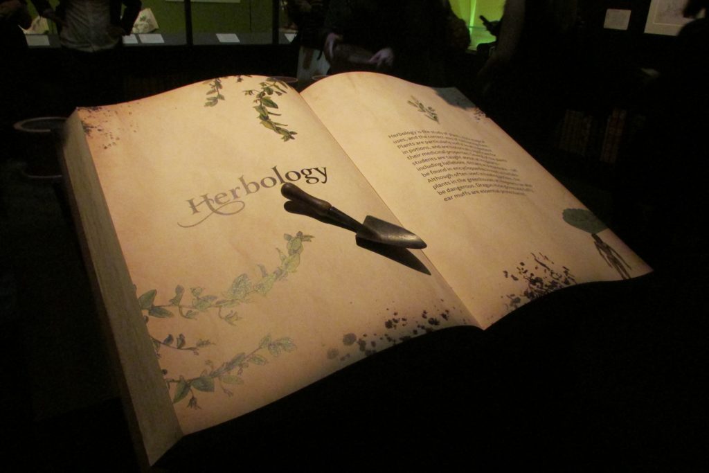 Livre ouvert introduisant la section botanique de l'exposition Harry Potter de la British Library avec une petite pelle de jardinage dessus